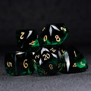 Puede incluir: Un conjunto de seis dados verdes y dorados con números negros. Los dados son de diferentes formas y tamaños.