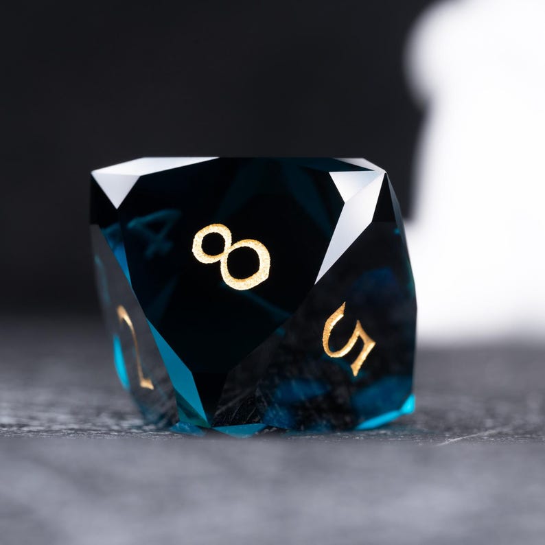 May include: A dark blue, faceted, crystal dice with gold numbers. The dice shows the number eight.