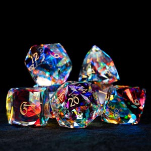 May include: A set of six iridescent dice with gold numbers. The dice are made of clear crystal and have a rainbow effect. The numbers on the dice are 6, 8, 12, 14, 20, and 4.