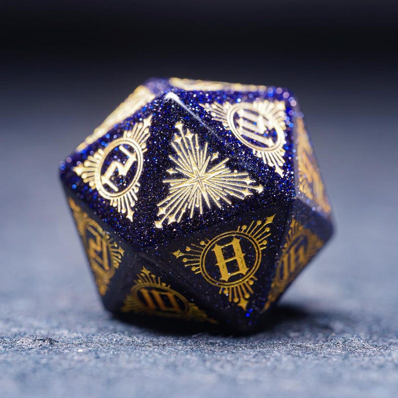 Op de afbeelding: Een blauwe en gouden polyhedrale dobbelsteen met een stervormig ontwerp en de nummers 1 tot en met 6 op elk vlak.