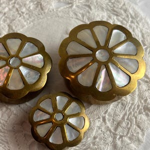 May include: Three decorative brass boxes with a floral design. Each box features a brass frame with a mother-of-pearl inlay. The boxes are in varying sizes, with the largest measuring approximately 7.6 cm in diameter.