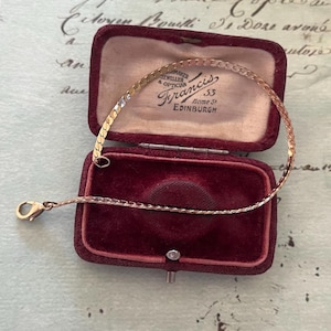 Könnte beinhalten: Ein goldenes Kettenarmband in einer roten Samtbox. Die Box trägt die Aufschrift "Juwelier & Optiker Francis 53 Home St Edinburgh".