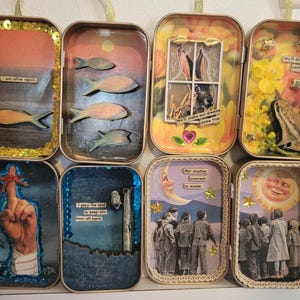 May include: A collection of eight decorative tin boxes, each with unique mixed-media art. The boxes feature various themes, including fish, a rabbit, a frog, a hand, and a group of people. The boxes are embellished with sequins and other decorative elements.