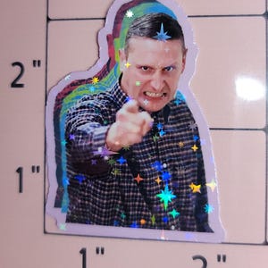 May include: Holographic sticker featuring a man pointing with an angry expression. The sticker has a layered effect with a purple outline and iridescent star accents. The man is wearing a plaid shirt.