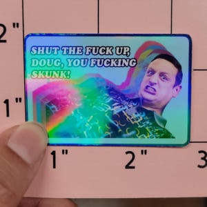 May include: A rectangular sticker with a holographic background and the text "SHUT THE FUCK UP, DOUG, YOU FUCKING SKUNK!". The sticker features a man with an angry expression and rainbow-colored effects.