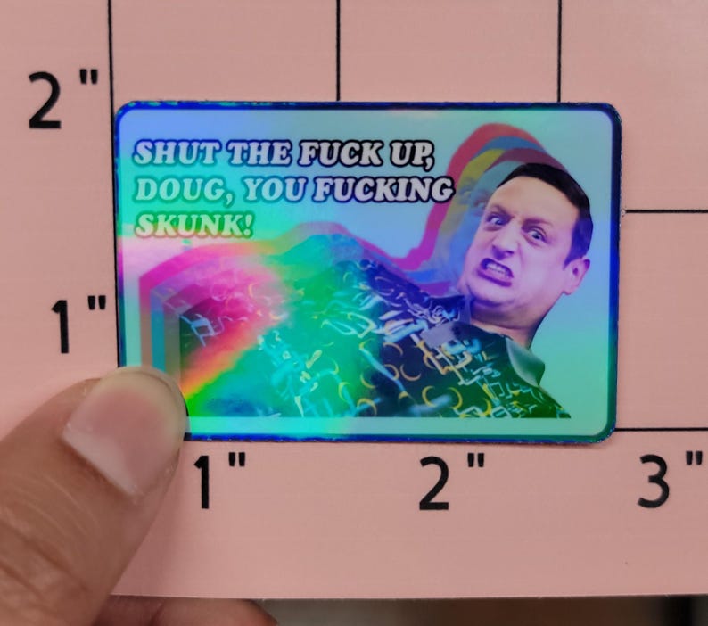 May include: A rectangular sticker with a holographic background and the text "SHUT THE FUCK UP, DOUG, YOU FUCKING SKUNK!". The sticker features a man with an angry expression and rainbow-colored effects.
