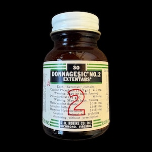 May include: A vintage amber glass medicine bottle with a white screw-top lid and a cream-coloured label. The label features the text Donnagesic No. 2 Extentabs, a list of ingredients including Codeine Phosphate, and a large red handwritten number 2.