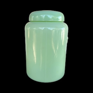 May include: A pale green glass jar with a matching lid. The jar has a rounded body and a smooth, glossy finish. The lid sits securely on top, creating a complete seal. The jar is a solid colour and has a simple, classic design.