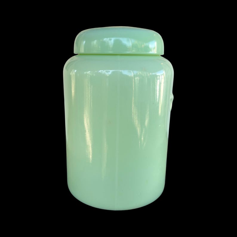 May include: A pale green glass jar with a matching lid. The jar has a rounded body and a smooth, glossy finish. The lid sits securely on top, creating a complete seal. The jar is a solid colour and has a simple, classic design.