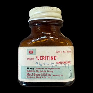 May include: A vintage amber glass medicine bottle with a white screw-top lid. The white label features red and teal text reading 'LERITINE', 'ANILERIDINE', '25 mg.', 'WARNING: May be habit forming', and 'Merck Sharp & Dohme' with handwritten ink.