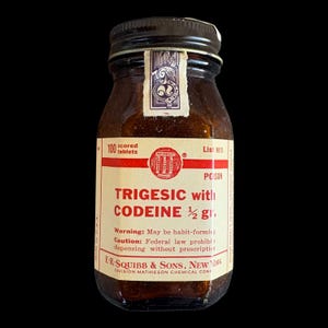 Puede incluir: Un frasco de vidrio ámbar vintage con tapa de rosca negra y sello de papel. La etiqueta de color crema presenta texto rojo que dice TRIGESIC with CODEINE 1/2 gr., 100 scored tablets, List 9815 y E.R. SQUIBB & SONS, NEW YORK.
