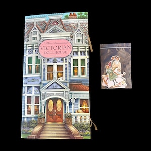 May include: A three-dimensional Victorian doll house book with a blue and white facade, featuring a front porch, stairs, and the text A Three-Dimensional VICTORIAN DOLL HOUSE 1890. Beside it is a small clear plastic bag containing paper doll cutouts.