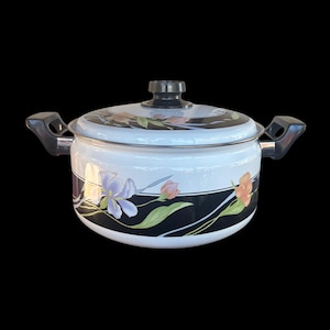 May include: White enamel cooking pot with a black rim and lid, featuring a floral design with purple, pink, and orange flowers. The pot has black handles and a black knob on the lid. A decorative kitchen item.
