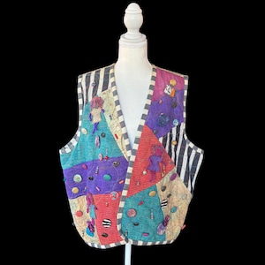 May include: A sleeveless vest featuring a patchwork design of multicolored fabric panels in teal, purple, red, and beige, accented with black and white striped trim. The garment is embellished with various buttons and small fabric doll figures.