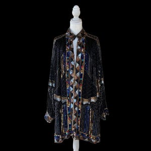 May include: A long-sleeved black jacket featuring intricate beadwork and sequins in shades of blue, gold, and silver. The garment displays a central vertical panel with a diamond pattern, flanked by linear and geometric beaded designs throughout.