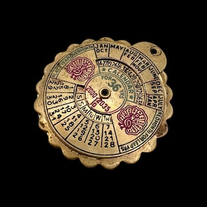 May include: A vintage brass calendar for 36 years, featuring rotating discs with months, dates, and leap year indicators. The calendar has a circular design with a scalloped edge and decorative floral accents in red and green.