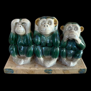 May include: A ceramic figurine set featuring three monkeys sitting on a rectangular base. The monkeys have cream-colored faces and feet with dark green glazed bodies. One monkey covers its eyes, one covers its ears, and one covers its mouth.
