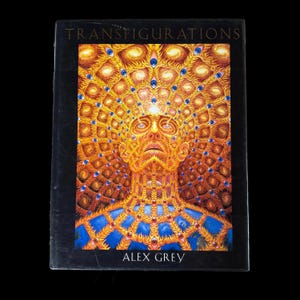 Könnte beinhalten: Ein Buch mit dem Titel "TRANSFIGURATIONS" von Alex Grey. Das Cover zeigt eine detaillierte Illustration einer menschlichen Figur mit einem komplizierten Augenmuster. Das Kunstwerk verwendet ein goldgelbes und blaues Farbschema.