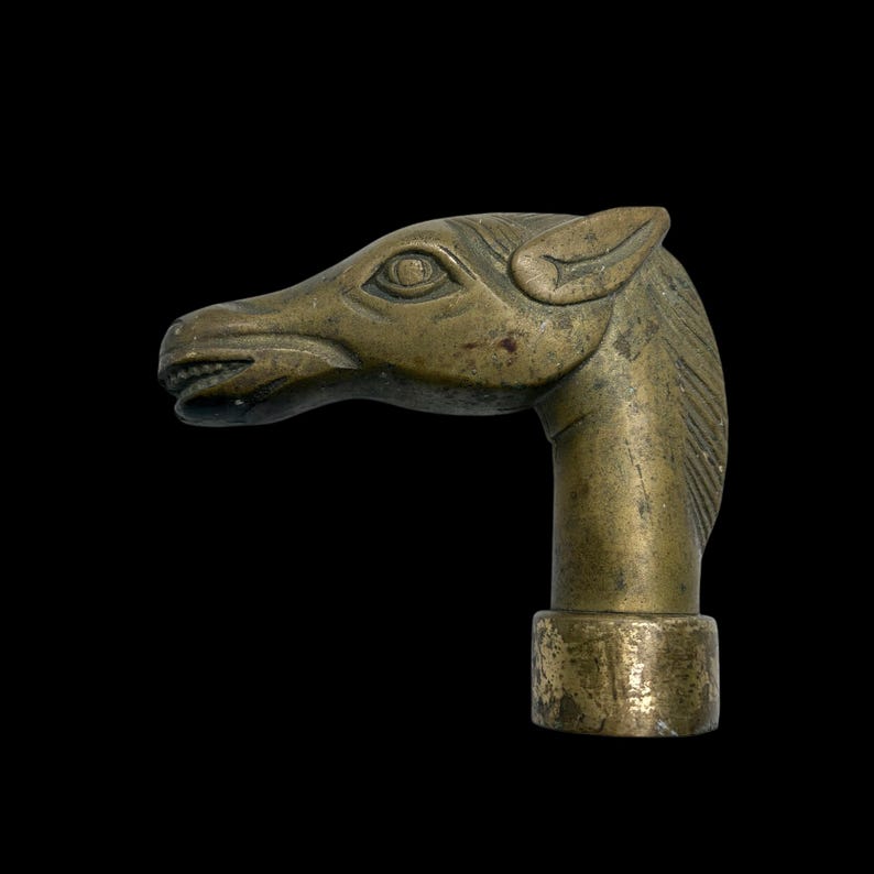 May include: A brass horse head cane topper. The horse's head is detailed with a textured mane and a stylized eye.