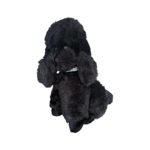 Può includere: Un giocattolo di peluche a forma di cane barboncino nero con un pelo soffice, orecchie flosce e un piccolo collare decorativo. Il giocattolo è seduto in posizione eretta, mostrando i suoi dettagli e il design realistico. La pelliccia del cane è di colore nero.