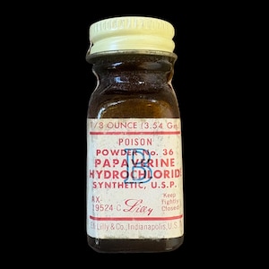 Puede incluir: Un frasco pequeño de vidrio ámbar con tapa de rosca color crema. La etiqueta blanca presenta texto rojo que dice POISON, POWDER No. 36, PAPAVERINE HYDROCHLORIDE, SYNTHETIC, U.S.P., 1/8 OUNCE (3,54 Gm.) y Eli Lilly & Co., Indianapolis, U.S.A.