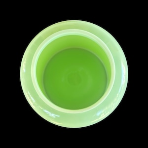 May include: A light green, circular container viewed from above, with a bright green interior. The container has a wide rim and a smooth, glossy finish. The background is black, accentuating the container's shape and colour.