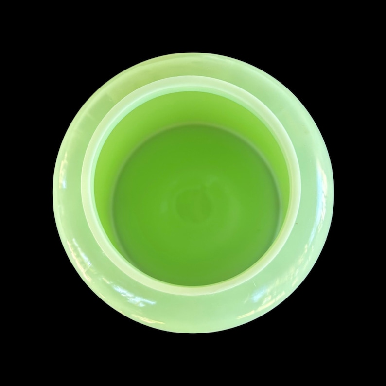 May include: A light green, circular container viewed from above, with a bright green interior. The container has a wide rim and a smooth, glossy finish. The background is black, accentuating the container's shape and colour.