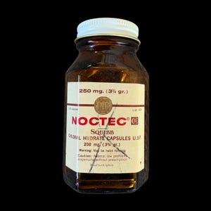 Puede incluir: Un frasco de medicina vintage de vidrio ámbar con tapa de rosca blanca. La etiqueta dice NOCTEC, SQUIBB, CHLORAL HYDRATE CAPSULES U.S.P., 250 mg. (3 3/4 gr.), 100 capsules, List 6205, con texto de advertencia y una X negra dibujada a mano.