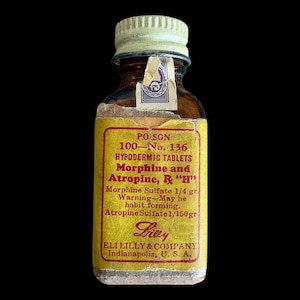 May include: A small amber glass bottle with a ribbed white screw cap and a yellow paper label. The label features red text reading POISON, 100-No. 136, HYPODERMIC TABLETS, Morphine and Atropine, R "H", Morphine Sulfate 1/4 gr, and Atropine Sulfate 1/150 gr.