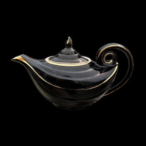 Puede incluir: Una tetera de cerámica negra con detalles dorados. La tetera tiene un pico curvo, un asa en forma de lazo y una tapa con un adorno. Los detalles dorados acentúan los bordes y detalles, creando un contraste llamativo.