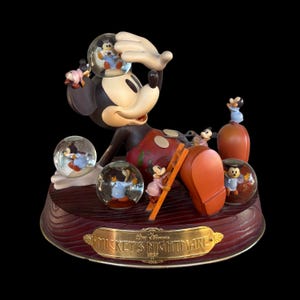 Könnte beinhalten: Eine Mickey-Mouse-Figur mit mehreren Schneekugeln. Die Figur ist schwarz, weiß, rot und gelb. Der Sockel ist braun mit einer goldenen Plakette mit der Aufschrift "Mickey's Nightmare". Die Schneekugeln enthalten Miniatur-Mickey-Mouse-Figuren.