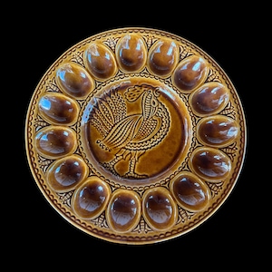 Może przedstawiać: Brązowy ceramiczny talerz do serwowania jajek z 12 wgłębieniami na jajka na obrzeżu. Środek przedstawia szczegółowy relief ptaka. Talerz ma błyszczące wykończenie i dekoracyjne obramowanie.