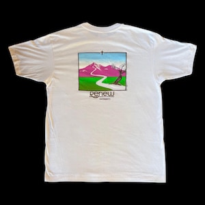 May include: A white short-sleeve t-shirt featuring a rectangular graphic on the back. The design depicts a pink mountain, a green field, a winding path, a tree, and a cross. Below the graphic, the text reads RENEW SACRAMENTO in brown lettering.