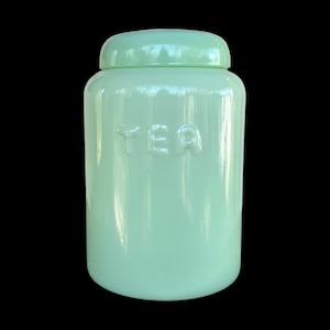 May include: A pale green ceramic tea canister with a matching lid. The word "TEA" is embossed on the front. The canister has a glossy finish and a rounded shape. A classic kitchen storage item.