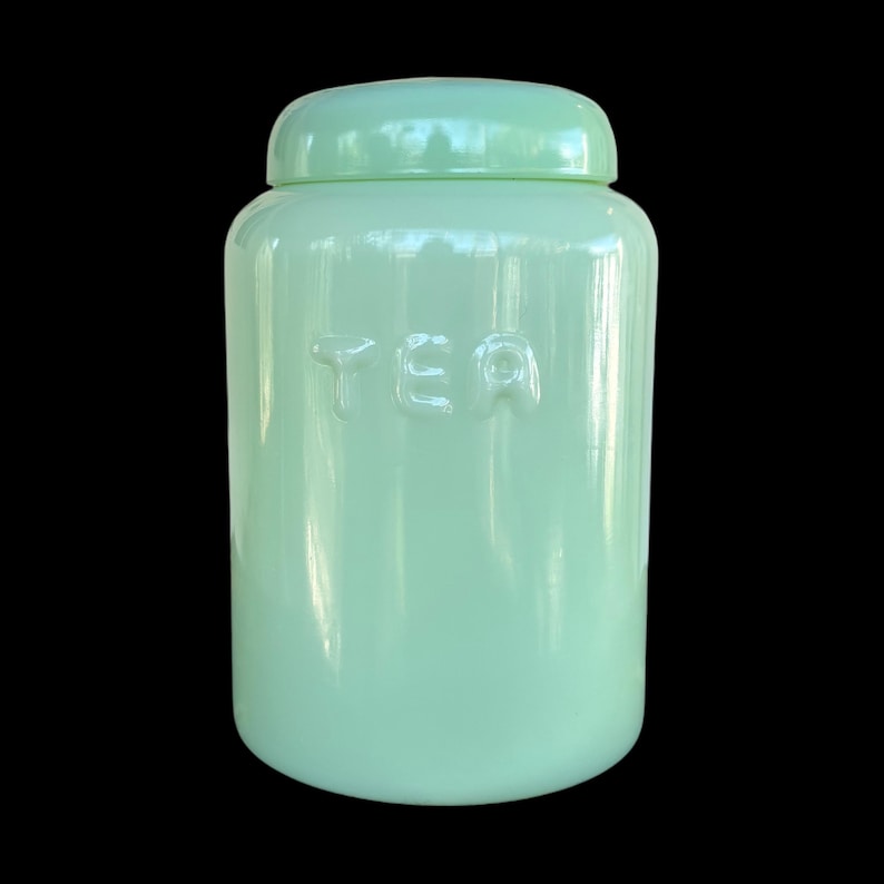 May include: A pale green ceramic tea canister with a matching lid. The word "TEA" is embossed on the front. The canister has a glossy finish and a rounded shape. A classic kitchen storage item.