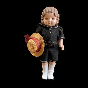 以下が含まれることがあります： 黒い服に白いトリム、白い靴下、白い靴を履いたヴィンテージドール。赤いリボンが付いた麦わら帽子を持っています。人形は茶色の髪で、黒い背景にあります。