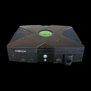 May include: Black Xbox video game console with the word "XBOX" in white lettering. The console has a green circular power button and a disc tray. The top of the console has a ridged design.