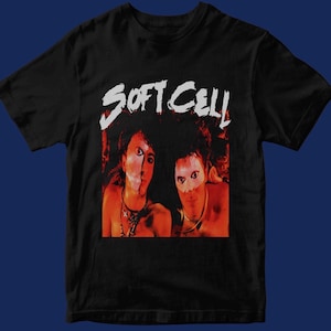 Op de afbeelding: Zwart T-shirt met een witte afbeelding van de band Soft Cell. De afbeelding toont twee mannen met rode en oranje gezichten en witte ogen.