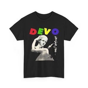 Könnte beinhalten: Ein schwarzes T-Shirt mit kurzen Ärmeln, das oben das Wort DEVO in roten, grünen, gelben und blauen Buchstaben zeigt. Unter dem Text befindet sich eine weiße Grafik einer klassischen Statuenbüste mit dem handschriftlichen Text come back jone... rechts.