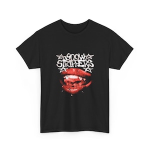 Op de afbeelding: Zwart t-shirt met een afbeelding van rode lippen met hoektanden en piercings, en de tekst "Snow Strippers" in witte, gestileerde letters. Het ontwerp is gecentreerd op de voorkant van het shirt.