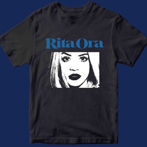 May include: A black t-shirt with a white graphic of a woman's face and the text "Rita Ora" in blue letters.