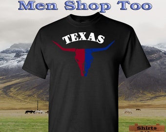 Peut inclure: T-shirt noir avec un texte "TEXAS" blanc au-dessus d'un crâne de taureau longhorn rouge et bleu. Le t-shirt est présenté sur un fond de chaîne de montagnes et de champ herbeux.