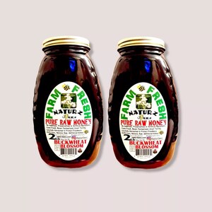 Peut inclure: Deux pots en verre de miel, chacun contenant 2 livres de miel de fleurs de sarrasin. Les pots sont &eacute;tiquet&eacute;s "Farm Fresh Naturz Beez Pure Raw Honey" et pr&eacute;sentent une &eacute;tiquette verte et blanche avec une illustration d'abeille.