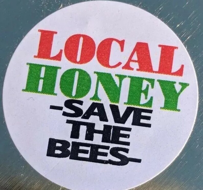 Peut inclure: Un autocollant rond blanc avec le texte "LOCAL HONEY - SAVE THE BEES" en lettres rouges, vertes et noires.