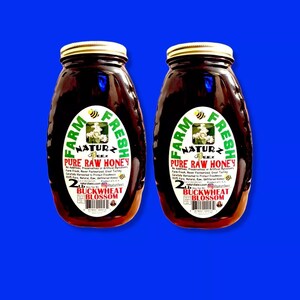 Peut inclure: Deux pots en verre de miel de fleurs de sarrasin cru. Les pots sont &eacute;tiquet&eacute;s "Farm Fresh Naturz Beez Pure Raw Honey" et pr&eacute;sentent une &eacute;tiquette verte et blanche avec une illustration d'abeille. Chaque pot contient 2 livres de miel.