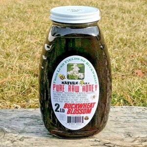 Peut inclure: Un pot en verre de miel fonc&eacute; avec un couvercle blanc. L'&eacute;tiquette indique "From Lush Fields of Buckwheat, Naturz Beez Pure Raw Honey, 2 lb Buckwheat Blossom".
