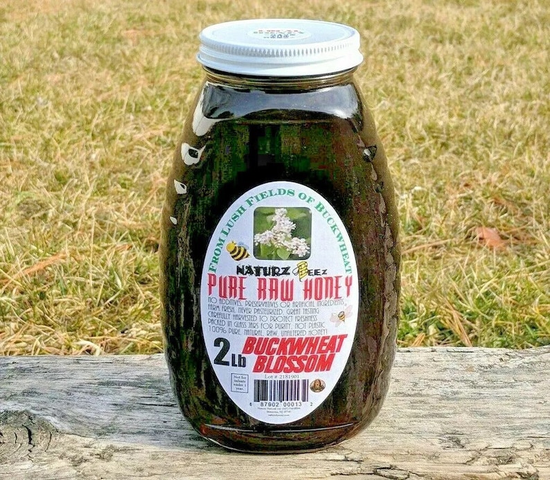 Peut inclure: Un pot en verre de miel fonc&eacute; avec un couvercle blanc. L'&eacute;tiquette indique "From Lush Fields of Buckwheat, Naturz Beez Pure Raw Honey, 2 lb Buckwheat Blossom".