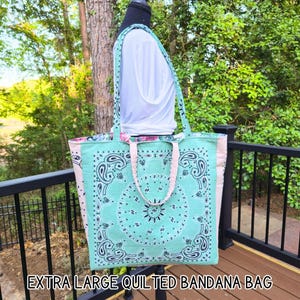 May include: An extra large quilted bandana bag in a turquoise paisley pattern with pink accents. The bag has a matching turquoise strap and the text "EXTRA LARGE QUILTED BANDANA BAG" at the bottom.