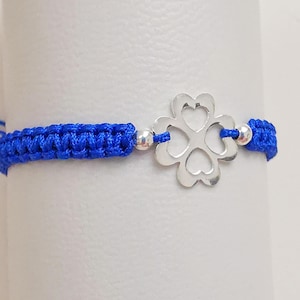 Puede incluir: Una pulsera trenzada azul con un dije de plata en forma de trébol de cuatro hojas.