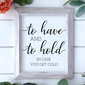 May include: White framed print with black calligraphy that reads "to have and to hold in case you get cold".